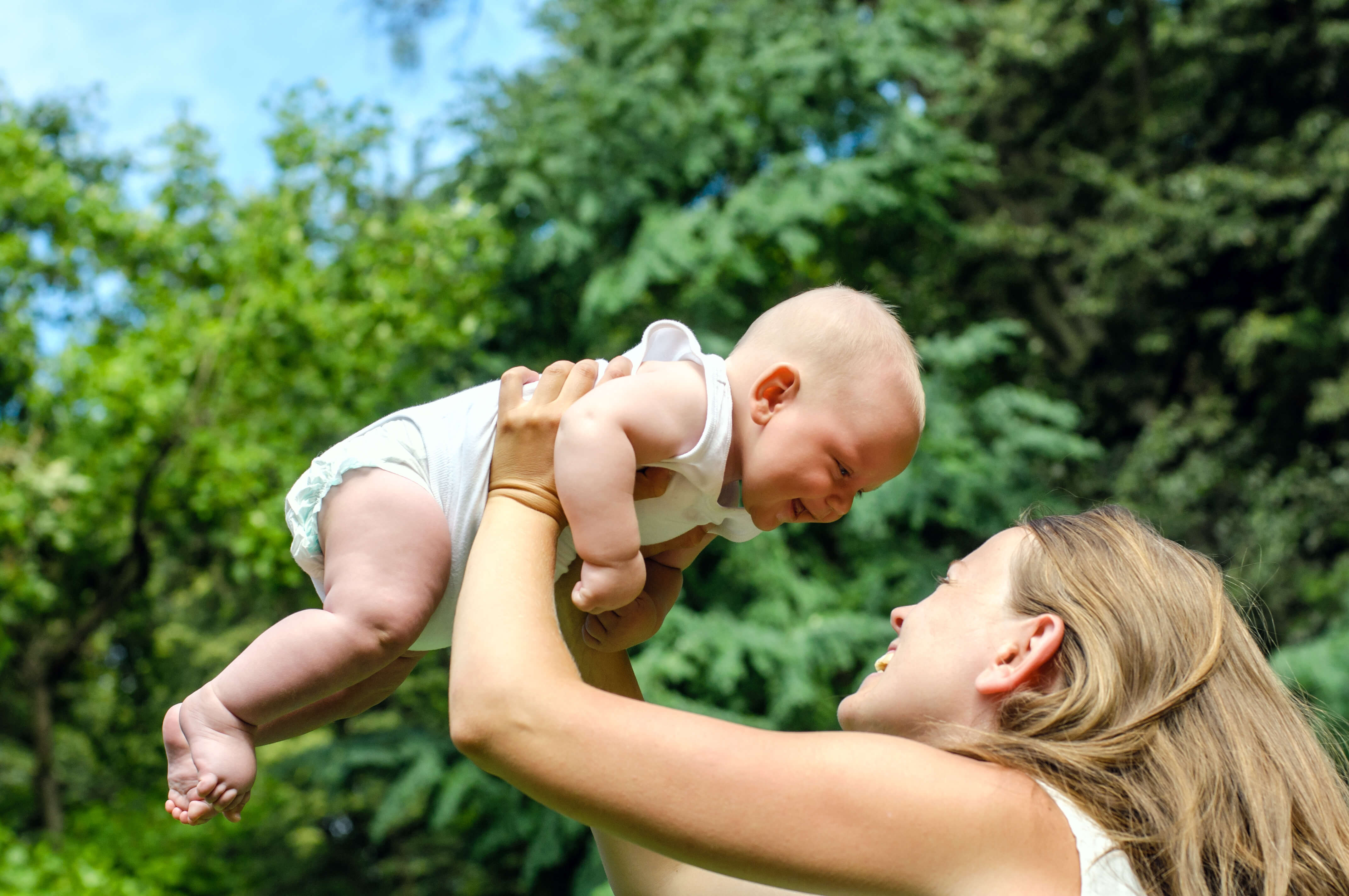 woman holding baby above her head outdoors