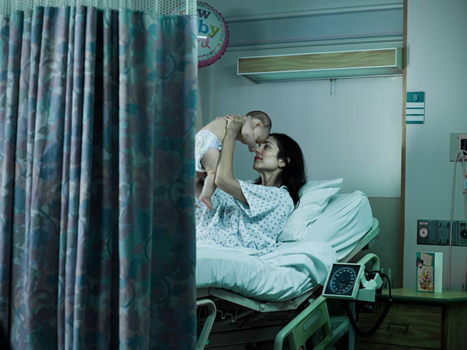 woman in a hospital bed and gown while holding an infant up