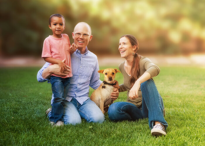 Happy family sitting on grass in yard with multi-ethnic child and dog