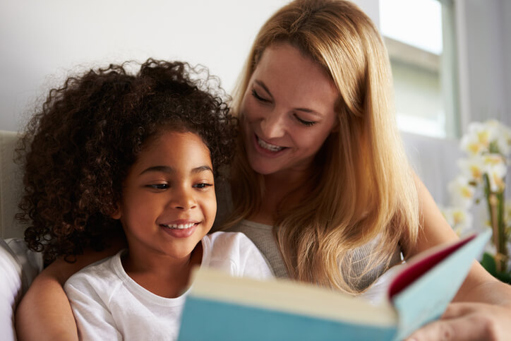 Caucasian mom and smiling black daughter read in bed, close-up